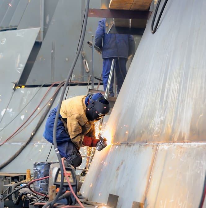 Welders working on a vertical steel segment of a ship