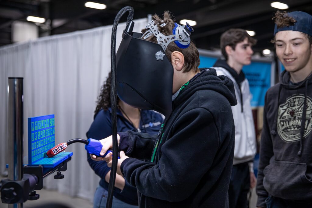 High school students practice their skills on a welding simulator at career fair.